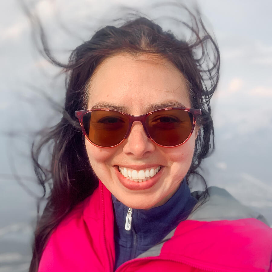 Headshot of autistic founder Layla Messner with her hair blowing in the wind. A brunette in a fuscia jacket and sunglasses.